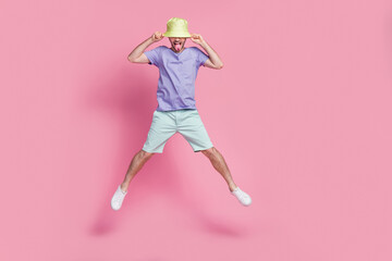 Full length photo of attractive young guy jump pull hat tongue out spread legs dressed trendy blue outfit isolated on pink color background