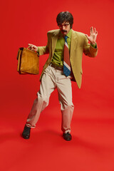 Portrait of stylish man with moustache posing in vintage suit dancing with briefcase isolated over...