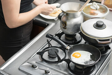 detailed view of a colombian kitchen with a woman preparing a typical breakfast. egg frying in a small frying pan on a gas stove.