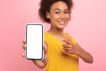 Smiling millennial african american curly woman point finger at phone with empty screen