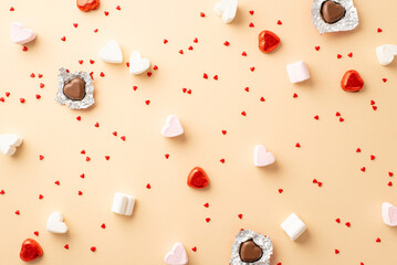 Valentine's Day concept. Top view photo of heart shaped chocolate candies and confetti on isolated beige background