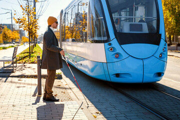 Fototapeta premium Blind man with a cane stopped on a tactile tile in front of a tram obstacle