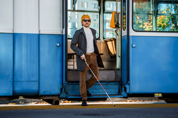 Blind man with a cane gets out of a tram at a public transport stop