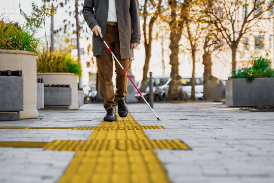Blind man with a walking stick. Walks on tactile tiles for self-orientation while moving through the streets of the city
