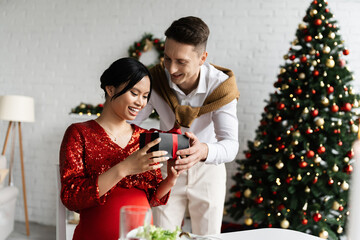 happy and pregnant asian woman taking Christmas present from young husband