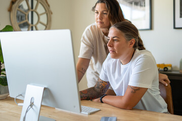 Adult lesbian couple work on desktop computer in home office