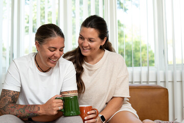 Adult lesbian couple sit on couch with coffee at home