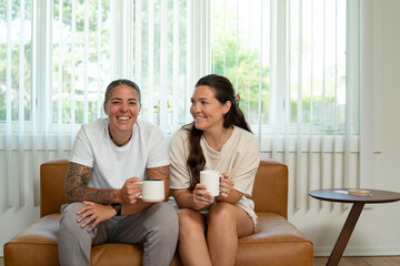 Obraz na płótnie Canvas Adult lesbian couple sit on couch with coffee at home