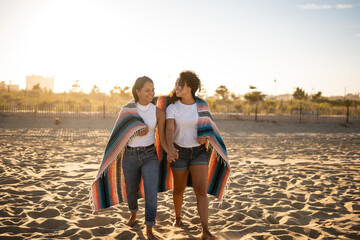 Hispanic lesbian couple walk with blanket at beach