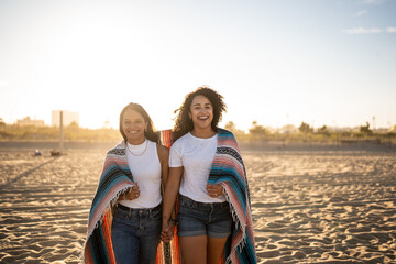 Fototapeta na wymiar Hispanic lesbian couple walk with blanket at beach