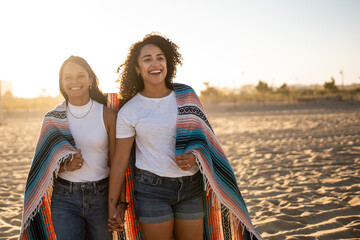 Hispanic lesbian couple walk with blanket at beach