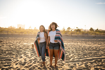 Fototapeta na wymiar Hispanic lesbian couple walk with blanket at beach