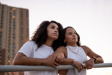 Hispanic lesbian couple lean on the railing at the boardwalk