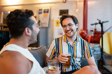 Two LGBTQ friends drink beer on a couch