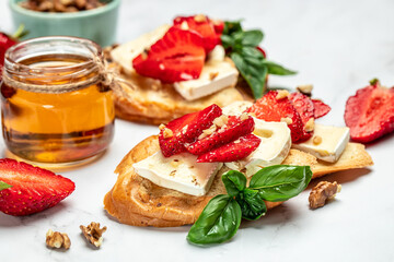 Bruschetta with strawberries, cheese camembert nuts and honey on a light background. banner, menu, recipe place for text, top view