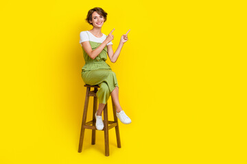 Full length photo of cute positive lady sitting chair fingers demonstrating new student cafeteria opening isolated on yellow color background