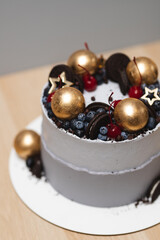 A beautiful single-tier cake with cheese cream, decorated with berries, cocktail cherries and golden chocolate balls