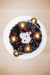 A beautiful single-tier cake with cheese cream, decorated with berries, cocktail cherries and golden chocolate balls