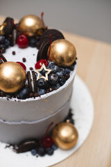 A beautiful single-tier cake with cheese cream, decorated with berries, cocktail cherries and golden chocolate balls