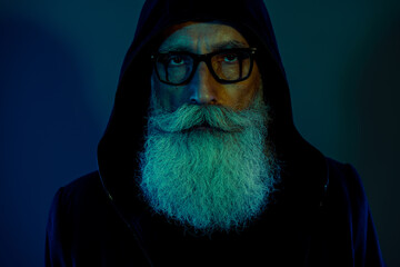 Photo of smart mysterious retired man dressed black pullover hood eyeglasses isolated dark blue...