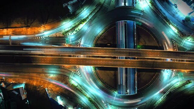Time-lapse of car traffic transportation on road at junction intersection, 4K. Aerial view of road interchange or highway intersection with busy urban traffic speeding on the road at night, IoT GPS 5g