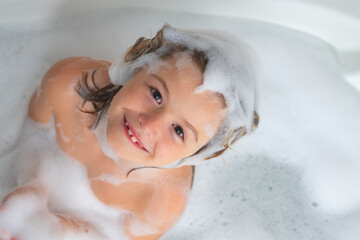 Kids shampoo. Foam on child head. Kid having fun in the bath with bubbles. Happy child enjoying...
