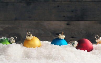 Colorful vintage Christmas baubles in the snow, wooden background with space for text
