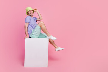 Full size photo of handsome young guy sit blank banner cube shopping promo dressed trendy blue garment isolated on pink color background