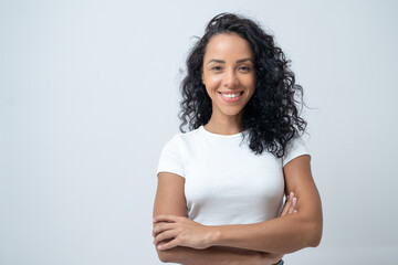 Obraz premium Portrait of smiling latin woman with curly hair with crossed arms isolated on grey background.