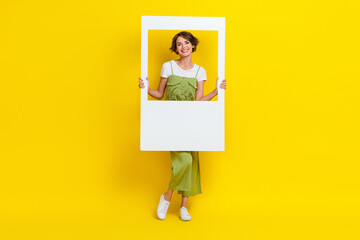 Full length photo of cute young lady toothy smile hold white instant photo frame dressed trendy...
