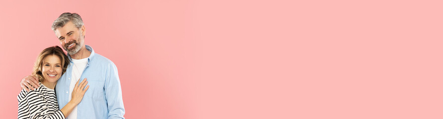 Fototapeta premium Happy middle aged couple embracing on pink studio background