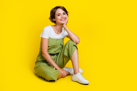 Full size photo of cute young girl sit floor relaxed listen interesting story wear trendy khaki clothes isolated on yellow color background