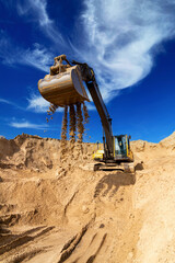 Yellow excavator working with sand at construction site