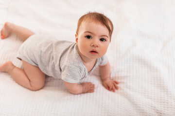 Cute little baby girl crawling on the bed and looking at camera, free copy space