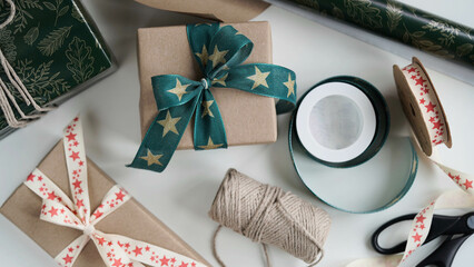 Gift boxes tied with beautiful ribbons with pattern stars with bow.Rolls wrapping paper,ribbons,rope,scissors,cones,red balls white background.Preparing for Christmas,New Year holidays,gift wrapping.
