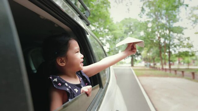 Little girl having fun to play with toy paper airplane out of car window