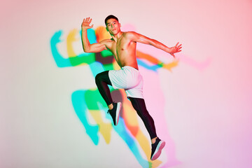 Portrait of young muscular man training, running isolated over pink background in neon light. Multicolored shadow.