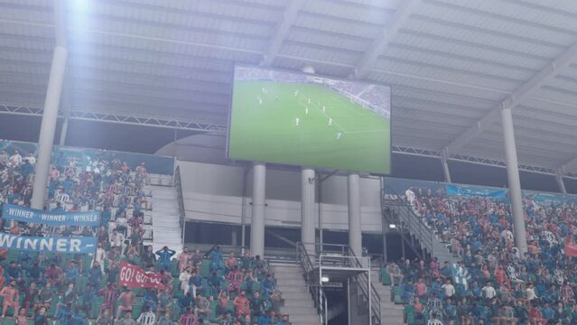 Football Soccer Championship Stadium Match, Scoreboard Screen Showing Repeat of the Goal. Crowd of Fans Cheering, Screaming, Having Fun. Sport Channel Television Advertising Playback