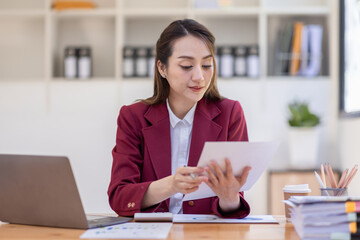 Asian woman working laptop in workplace, Business woman wearing red jacket suit busy working on laptop computer checking finances, investment, economy, saving money or insurance concept
