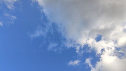Blue sky with cumulus clouds. Low cumulus clouds of various shapes and sizes float slowly across the blue sky. Clouds of white gray color illuminated by the sun's rays.