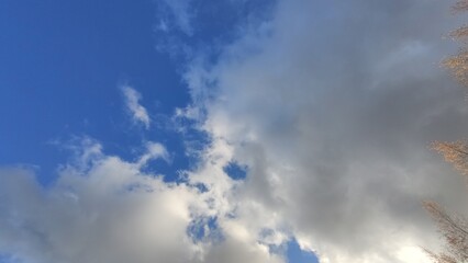 Blue sky with cumulus clouds. Low cumulus clouds of various shapes and sizes float slowly across the blue sky. Clouds of white gray color illuminated by the sun's rays.