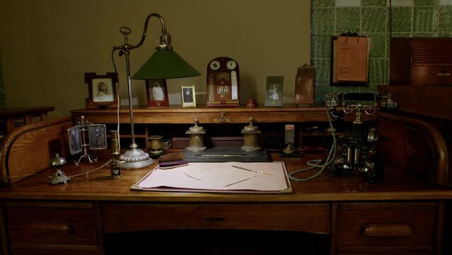 Vintage desk with writing utensils, lamp, old phone, photos.