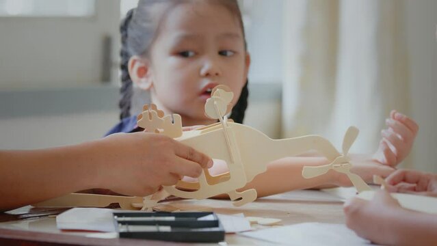 Asian girl is modeling a wooden toy airplane with her parent assistance