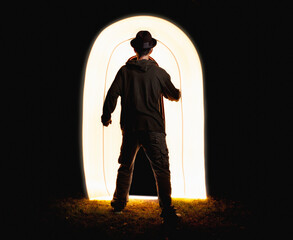 Abstraction, a man in a hat goes into another space through a luminous door, night, long exposure