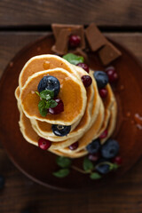Pancakes with berries are stacked. Pancakes poured with honey