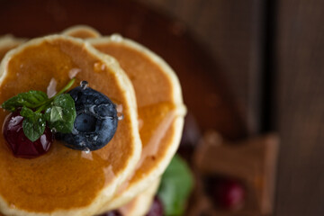 Pancakes with berries are stacked. Pancakes poured with honey