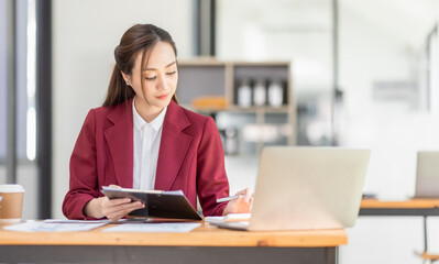 Asian Businesswoman Using laptop computer and working at office with calculator document on desk, doing planning analyzing the financial report, business plan investment, finance analysis concept.