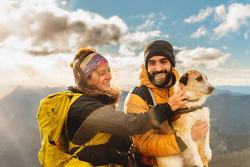 couple of hikers in the rain making a mountain route with their dog. Mountaineer holding his dog in his arms with a mountain range landscape in the background. woman petting dog