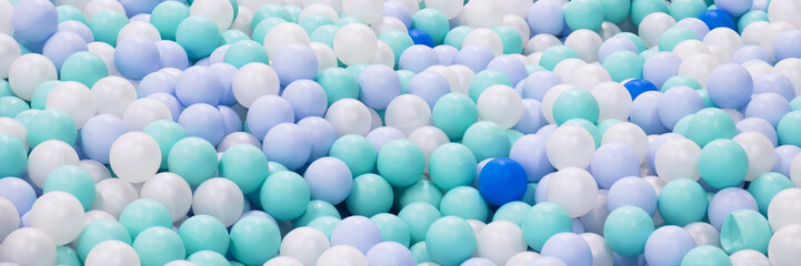 Abstract background from plastic balls of white, blue and green colors. Pool with plastic balls in the children's entertainment center. Pastel delicate colors, selective focus. Banner, letterhead