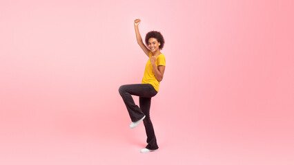 Happy millennial african american curly woman student in casual rejoices, makes gesture of victory and success